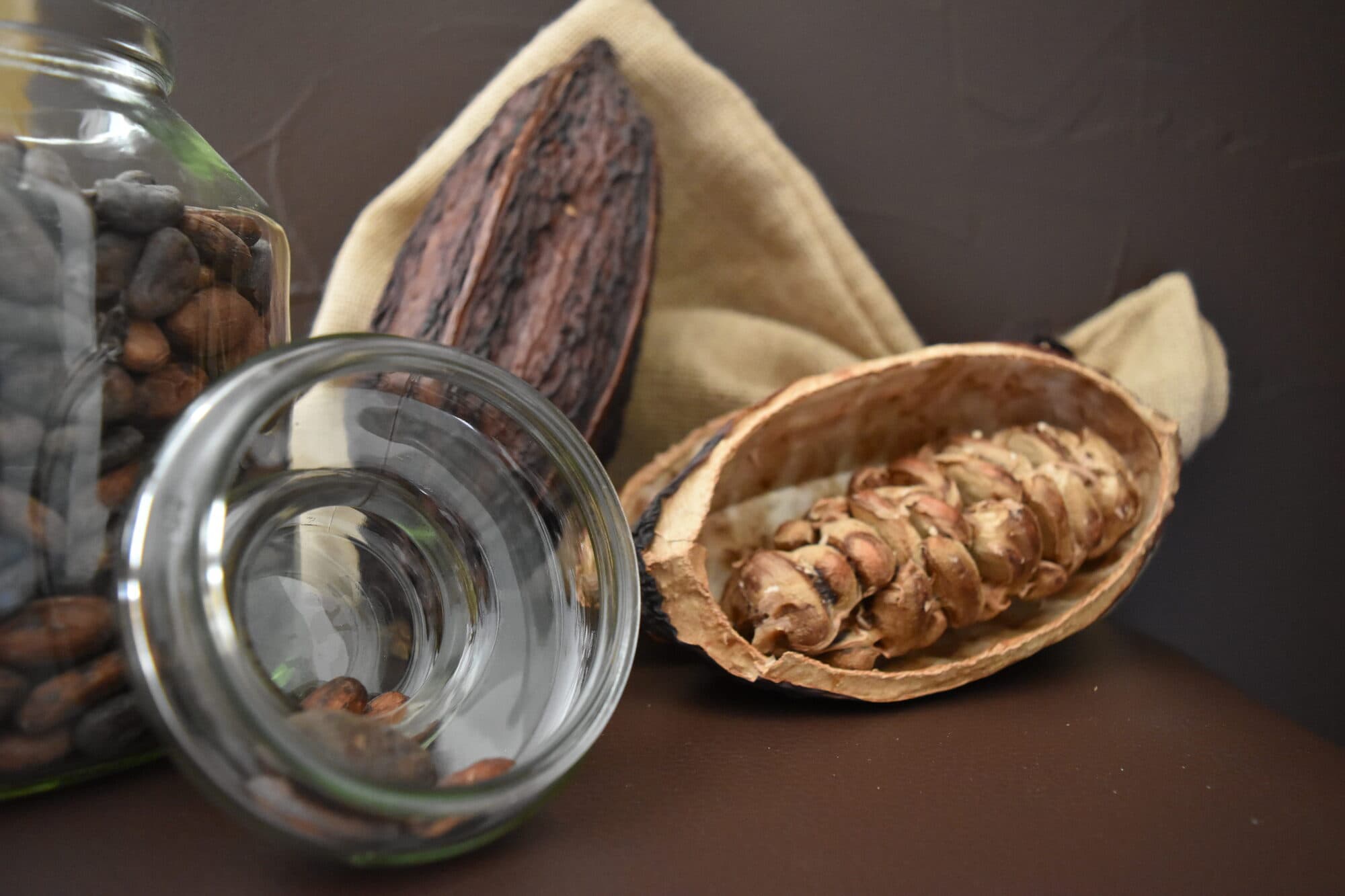 Fèves de cacao dans un bocal en verre, à côté d’une cabosse ouverte